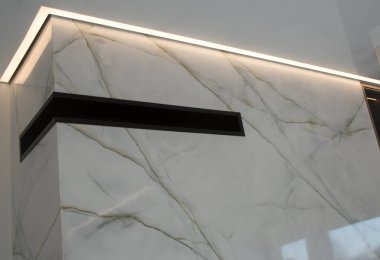 Beyaz mermerin altındaki gri damarlı panellerle çevrili duvar. Duvarın üst kısmında arka lambalı bir oyuk var, köşe boyunca yer alıyor. Çukur, siyah bir iç elementle dikdörtgen şeklindedir..