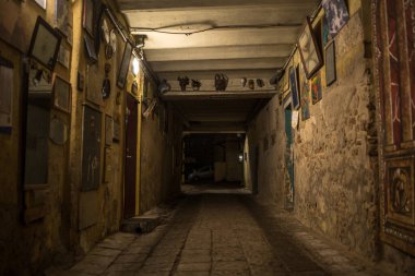 Vilnius Eski Kasabası 'ndaki uzun ve dar bir geçitin yatay fotoğrafı. Bahçenin duvarları eski, çatlak, sarımsı tonlarda boyanmış ve birçok resim, ayna ve farklı boyutlarda dekoratif elementlerle süslenmiş.