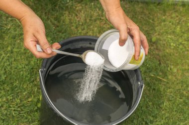 Bir insan su dolu bir kovaya gübre ekler. Madde bir eliyle tutulan büyük bir kaşıktan dökülür, diğer eliyse maddenin geri kalanıyla birlikte bir kap tutar..