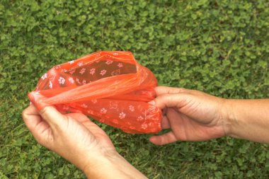 Birisi yerden köpek dışkısı toplamak için plastik torba kullanıyor. Bir el, torbaya sarılmış, dışkıyı tutuyor, ve diğer el de çantayı sıkıca kapatmaya yardım ediyor..