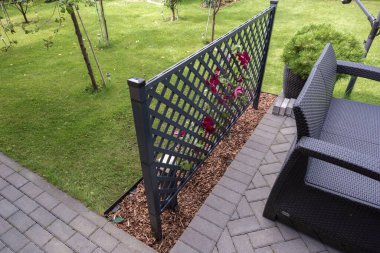 Özel bir evin terasının iyi döşenmiş bir köşesi. Peyzaj tasarımı elementleri görülebilir: samanla kaplanmış, ekilmiş çalılarla kaplı bir çiçek yatağı. Yakınlarda büyük bir tencere var..