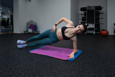 Kadın sporcu spor salonu ortamında spor yaparken spor yapıyor, vücut kaslarını çalıştırıyor ve dengeyi arttırıyor.