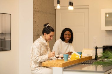 İki farklı kadın, keyifli bir anı paylaşıyor. Sıcak ve kahkahalarla dolu, parlak, modern bir mutfakta birlikte çikolatalı pastanın tadını çıkarıyorlar. Arkadaşlık ve hoşgörüyü kutluyorlar.