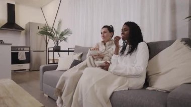 İki bayan arkadaş, bir beyaz ve bir Afrikalı Amerikalı modern evlerinde rahat bir kanepede rahatlar televizyonda büyüleyici bir film izlerken bir kase patlamış mısır paylaşırlar.