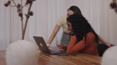 Gülümseyen, dizüstü bilgisayardaki proje detaylarını gözden geçiren, modern çalışma alanında yan yana oturan, profesyonel dostluk ve iş birliği ortamı sergileyen kadın meslektaşlar.