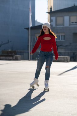 Young woman wearing a vibrant red sweater and cozy white beanie roller skating through an urban landscape, celebrating an active and healthy lifestyle with joy and freedom clipart