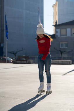 Young woman wearing a red sweater and white beanie enjoys roller skating on a sunny day in an urban environment, showcasing a carefree and active lifestyle clipart