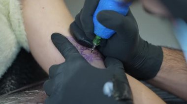 Profesyonel dövme sanatçısı siyah koruyucu eldivenler takıyor hassas dövme makinesi kullanarak müşterinin koluna detaylı mürekkep tasarımı uyguluyor, sanatsal beceri ve yaratıcı odaklanma gösteriyor