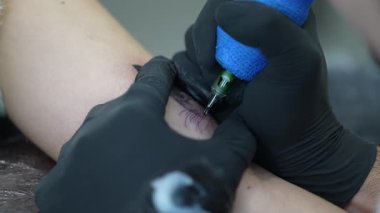 Siyah koruyucu eldivenler giyen profesyonel dövme sanatçısı, özel dövme ekipmanları kullanarak tüysüz kedi derisi üzerinde detaylı tasarım yapıyor.