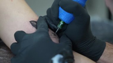 Profesyonel dövme sanatçısı, odaklanmış teknik ve tıbbi bakım ile steril stüdyo ortamında özel ekipman kullanarak kedilere siyah kalp dövmesi yapıyor.