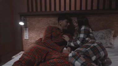 Aynı pijamaları giyen genç bir çiftin yavaş çekim videosu. Yatağa uzanmış, samimi anları paylaşıyor ve yumuşak ışıklı bir yatak odasında birlikte vakit geçiriyorlar.