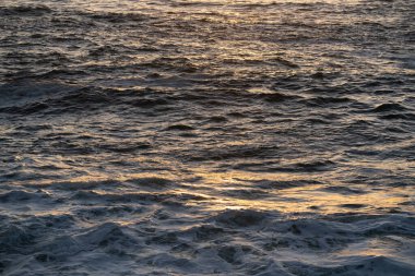 Altın gün batımı Punta Faxilda, Sardunya 'daki dalgalı okyanus yüzeyine yansıyarak çarpıcı ve sakin bir doğal deniz manzarası yaratıyor.