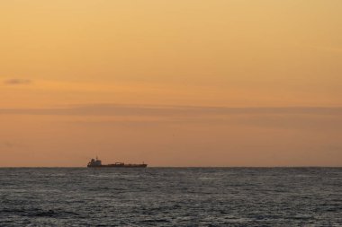 Büyük bir kargo gemisi sakin bir denizi sorunsuzca geçiyor. Güneş batarken Punta Faxilda yakınlarında çarpıcı bir turuncu gökyüzü tarafından aydınlatılıyor. Huzurlu ve pitoresk bir deniz manzarası oluşturuyor.