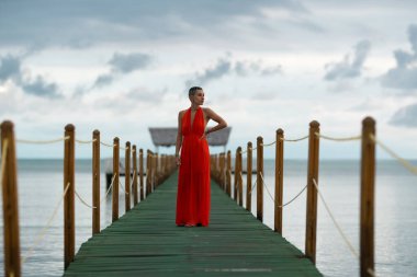 Uzun turuncu elbiseli genç bir kadın Cayo Guillermo, Küba 'da, okyanusun üzerinde ahşap bir iskelede yürüyor ve rahatlatıcı bir tatil kaçamağının tadını çıkarıyor.