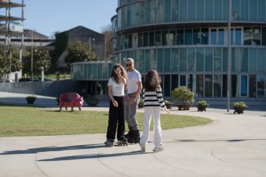 Mutlu bir aile şehir parkında güneşli bir günün tadını çıkarıyor. Baba iki kızına paten yapmayı öğretiyor. Sağlıklı yaşam tarzını, aile bağlarını ve açık havada eğlenmeyi destekliyor.