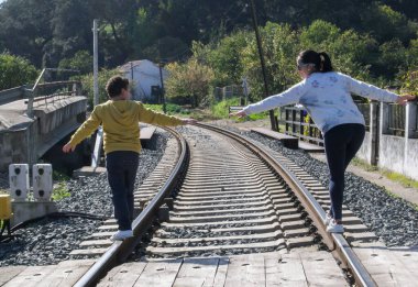 Genç kız sırtüstü oturmuş, güneşli bir günde dağlarda bir göle bakıyor.