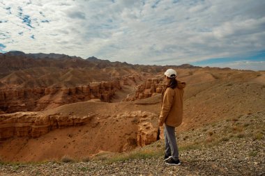 Yoldaki dişi turist güzel turuncu kanyon dağlarına ve bulutlu gökyüzüne bakıyor.