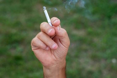 Bir adamın eli, yeşil çimenlerin arka planına karşı elinde bir sigara tutuyor..