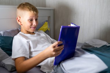 Sarışın genç çocuk yatmadan önce kitap okuyor.