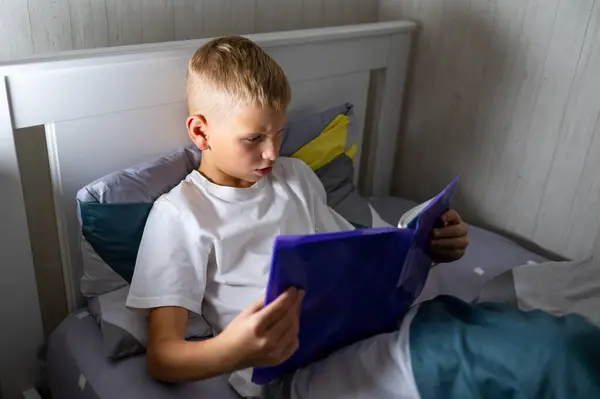 Sarışın genç çocuk yatmadan önce kitap okuyor.
