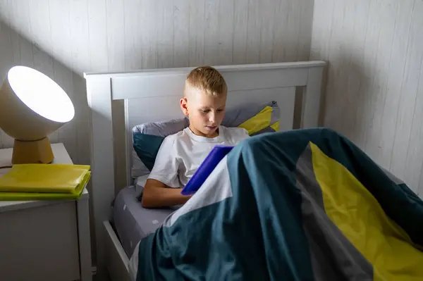 Sarışın genç çocuk yatmadan önce kitap okuyor.