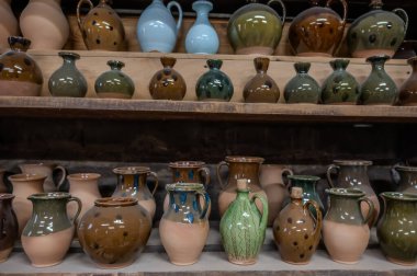 Kırsal ahşap raflarda sergilenen el yapımı seramik çömlek koleksiyonu. Çeşitli şekiller, boyutlar ve toprak renkleri içererek, geleneksel zanaatkarlık ve zanaat tasarımını ön plana çıkarıyor. Ilık aydınlatma, parlak parlaklığı arttırır. 