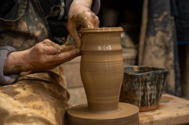 Islak kille kaplı bir çömlekçinin elleri, dönen bir çömlek çarkında uzun seramik bir vazo şekillendirirken.. 