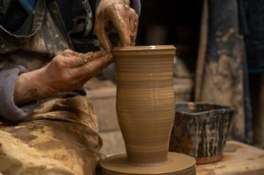 Islak kille kaplı bir çömlekçinin elleri, dönen bir çömlek çarkında uzun seramik bir vazo şekillendirirken.. 