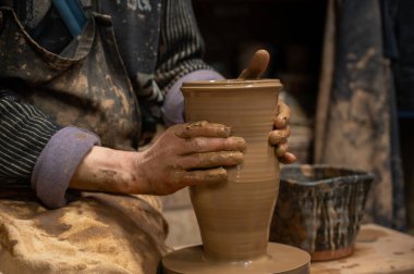 Islak kille kaplı bir çömlekçinin elleri, dönen bir çömlek çarkında uzun seramik bir vazo şekillendirirken.. 