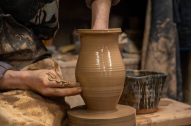 Islak kille kaplı bir çömlekçinin elleri, dönen bir çömlek çarkında uzun seramik bir vazo şekillendirirken.. 
