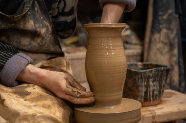Islak kille kaplı bir çömlekçinin elleri, dönen bir çömlek çarkında uzun seramik bir vazo şekillendirirken.. 
