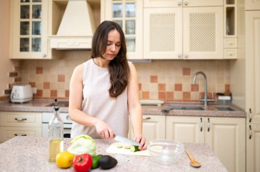 Mutfakta taze sebze salatası için salatalık kesen gülümseyen kadın. Sağlıklı yaşam tarzı, ev yemeği, diyet ve düzgün beslenme.