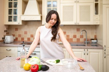 Genç bir kadın taze sebzelerle dolu bir masaya bakıyor ve salata yapmayı planlıyor. Sağlıklı yaşam tarzı, ev yemeği, diyet ve düzgün beslenme.