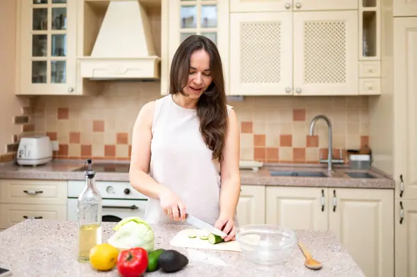 Mutfakta taze sebze salatası için salatalık kesen gülümseyen kadın. Sağlıklı yaşam tarzı, ev yemeği, diyet ve düzgün beslenme.