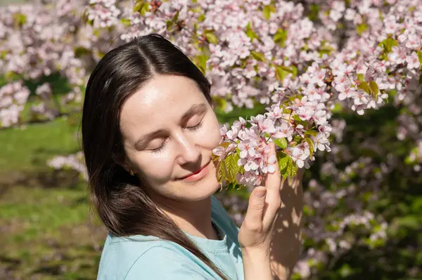 Gözleri kapalı genç bir kadın huzurlu bahar parkında kiraz çiçeklerinin kokusunun tadını çıkarıyor.