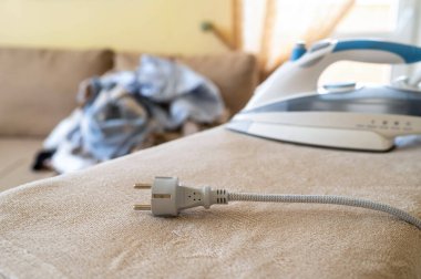 Elektrik kablosu ve ütü masasının fişi takılı fişi çekilmiş. Arka planda buruşuk çamaşırlar var.