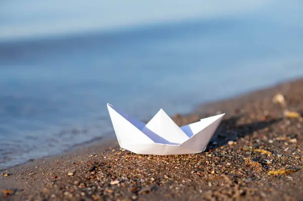 Göl kıyısındaki kağıttan tekne, sakin suların yanındaki ıslak kumda dinleniyor.