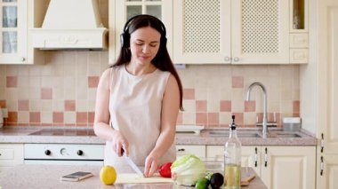 Genç bir kadın mutfak masasında taze salata yapıyor. Kadın evde sağlıklı yemek pişiriyor..