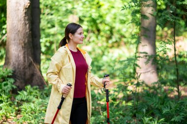 Güneşli ormanda yürüyüş direğiyle yürüyen bir kadın.