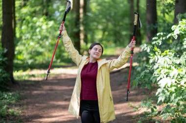 Ormandaki kadın İskandinav yürüyüş direklerini kaldırıyor, yalnızlığın ve doğayla bağın tadını çıkarıyor.