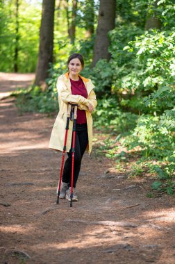 Ormanda elinde yürüyüş direkleri olan güzel bir kadının portresi. Açık hava macerası ve yürüyüş deneyimi için hazır.