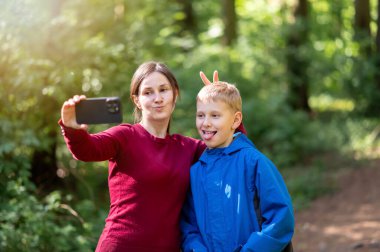 Anne ve oğlu bahar ormanı yürüyüşü sırasında selfie çekerken komik surat ifadeleri takınıyorlar, doğada eğlenceli aile zamanlarının tadını çıkarıyorlar.