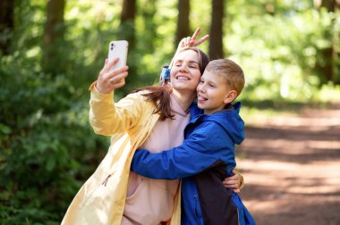 Mutlu anne ve oğul bahar parkında selfie çekiyor, çocuk surat asıyor ve dilini çıkarıyor.