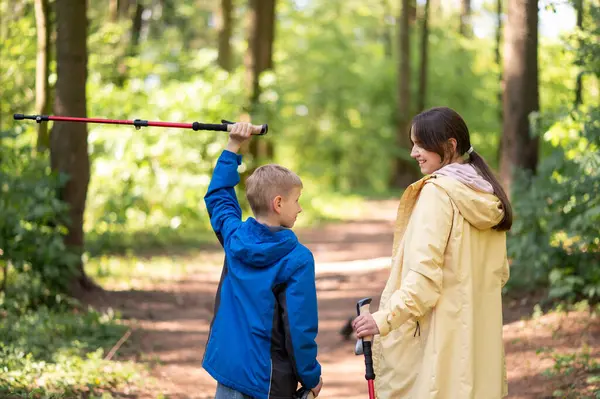 Kadın ve oğul güneşli bir orman yürüyüşü sırasında başlarının üzerinde İskandinav yürüyüş direklerini kaldırarak aktif aile zamanlarının keyfini çıkarıyorlar.