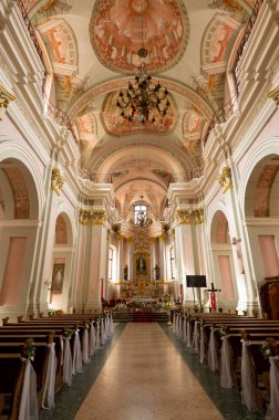 Uzun kilise sıraları ve büyük bir sunağı olan büyük bir kilise. Sıralar boş ve sunak çiçeklerle kaplı.