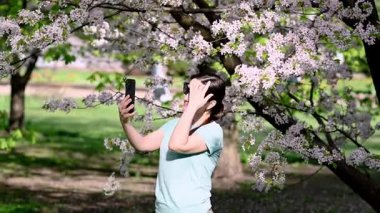 Bir kadın çiçek açan bahar parkında dokulara hapşırıyor, polen alerjisinden muzdarip.