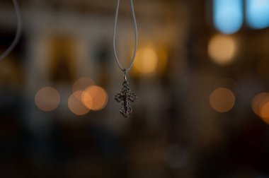 Yumuşak arkaplanlı bir ipe asılı Ortodoks haç kolyesi, inancın ve narin ışıkta ruhani bağlılığın sembolü.