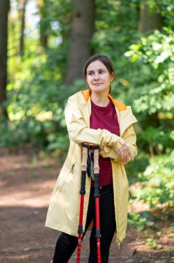 Ormanda elinde yürüyüş direkleri olan güzel bir kadının portresi. Açık hava macerası ve yürüyüş deneyimi için hazır.