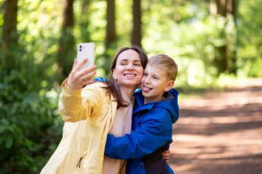 Mutlu anne ve oğul bir bahar parkında selfie çekerken dışarıda neşeli aile anlarının tadını çıkarıyorlar.