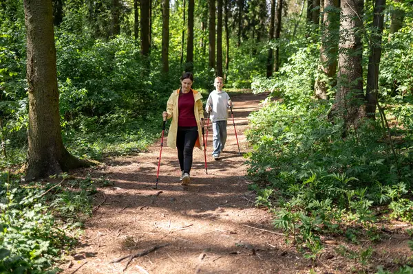 Anne ve oğlu güneşli bir ormanda yürüyor, dışarıda İskandinav yürüyüşü yapıyorlar.